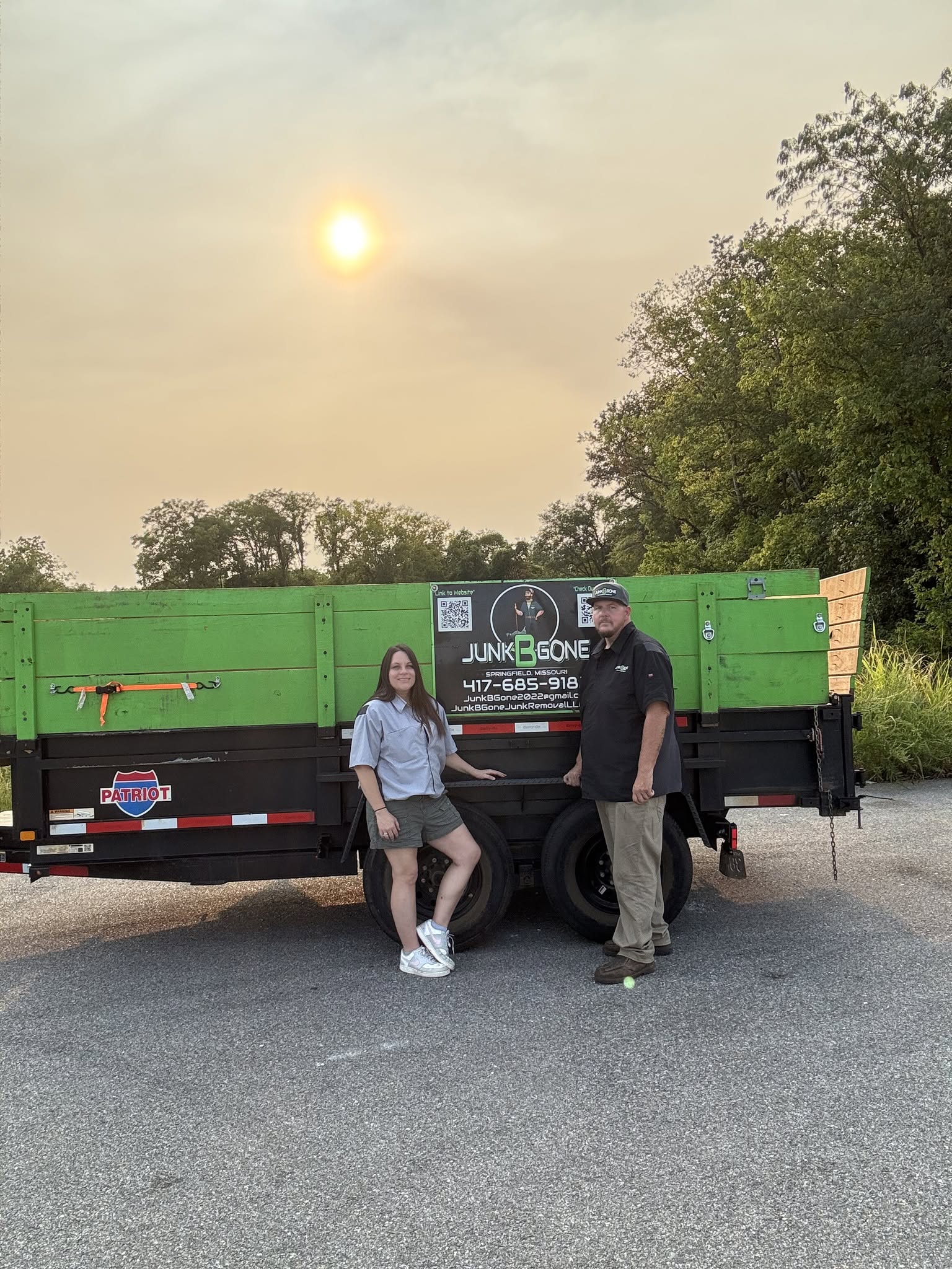 Junk B Gone owners with branded hauling trailer in {city}, {state}
